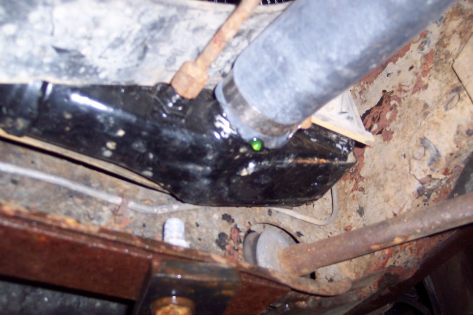 Close-up of rusted vehicle undercarriage with a black component and dripping green fluid.