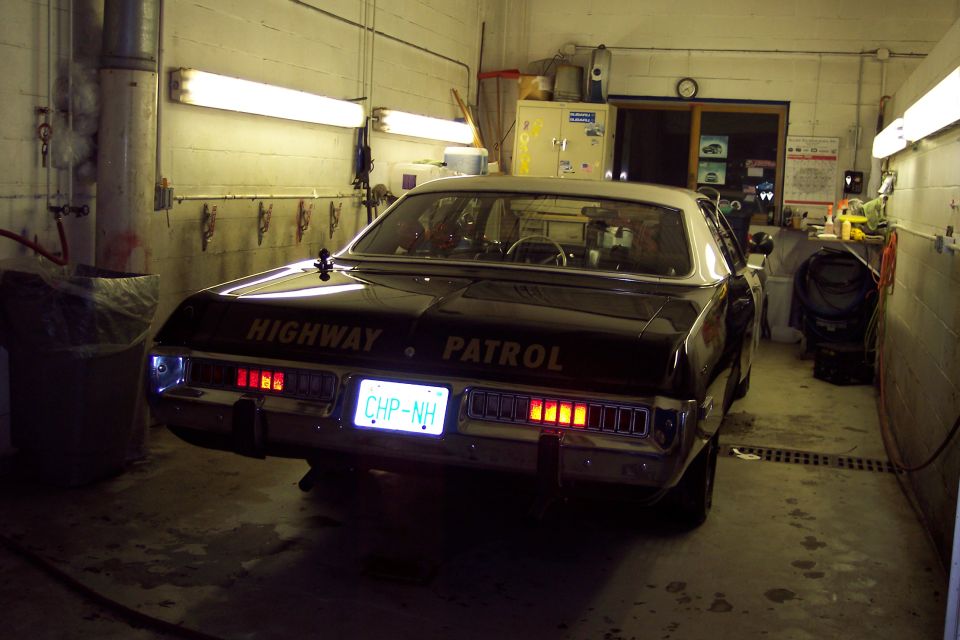 Rear view of a black and white highway patrol car with license plate CHP-NH in a garage.