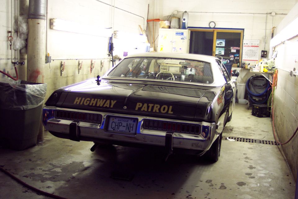 Rear view of a black and white highway patrol car with gold lettering and NH license plate in a garage.