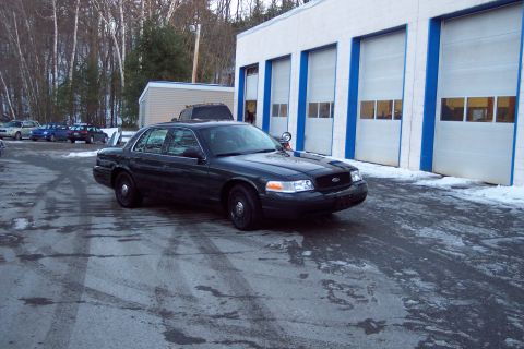 2001 Ford Crown Victoria - A dark 2001 Ford Crown Victoria is parked in front of a building with garage doors.