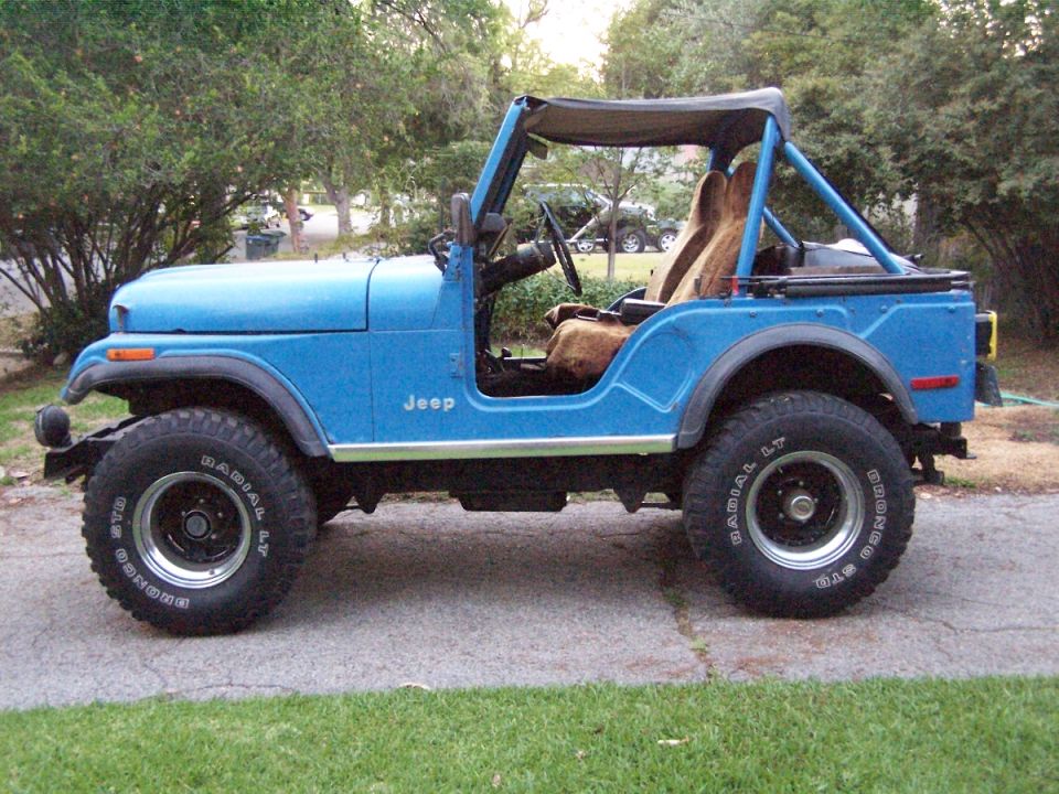 Blue Jeep CJ-5 in side profile on a driveway with soft top rolled back