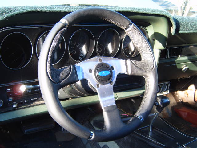 Close-up of a classic car interior, showing a custom steering wheel and dashboard gauges.