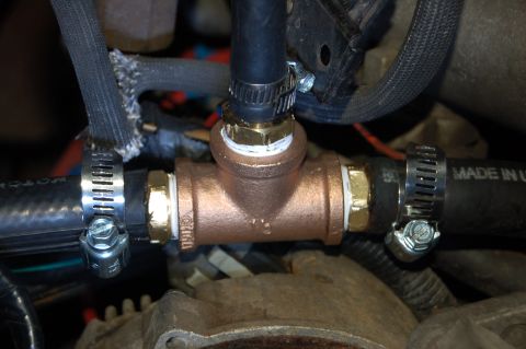 1989 Ford Bronco - A close-up view shows a bronze T-fitting connecting two black hoses, secured by metal hose clamps. White sealant is visible around the thre…