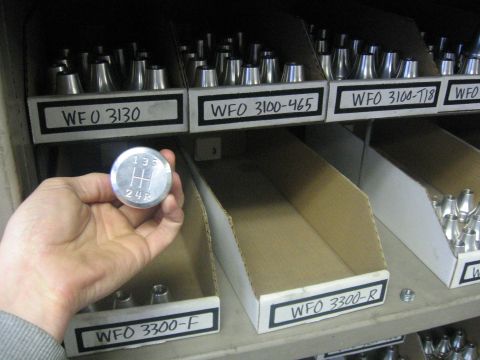 1989 Ford Bronco - Photo of a hand holding a shifter knob in front of labeled parts bins, not a technical document.