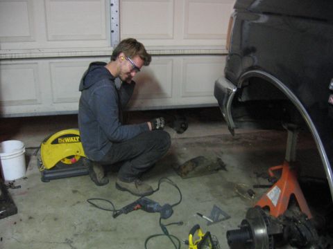 1989 Ford Bronco - A man works on the undercarriage of a black SUV in a garage, surrounded by tools and car parts.