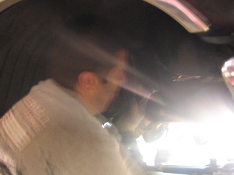 1989 Ford Bronco - A person is working on the undercarriage of a vehicle, with bright light making details difficult to discern.