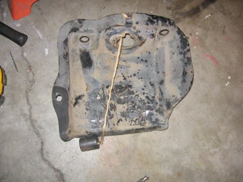 1989 Ford Bronco - A dirty metal skid plate, possibly from a vehicle, with a string and weight attached.