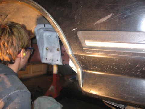 1989 Ford Bronco - A person works on a metal bracket attached to the side of a dark vehicle.