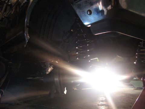 1989 Ford Bronco - The undercarriage of a vehicle is visible, with a bright light illuminating the suspension and tire area around the wheel.