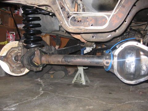 1989 Ford Bronco - The rear axle assembly and suspension components of a vehicle are visible, supported by jack stands in a garage.