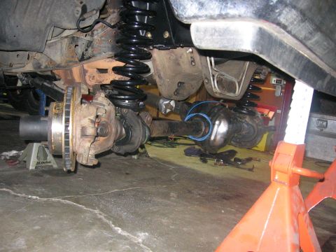 1989 Ford Bronco - The underside of a vehicle is shown with suspension and drivetrain components exposed, supported by jack stands.