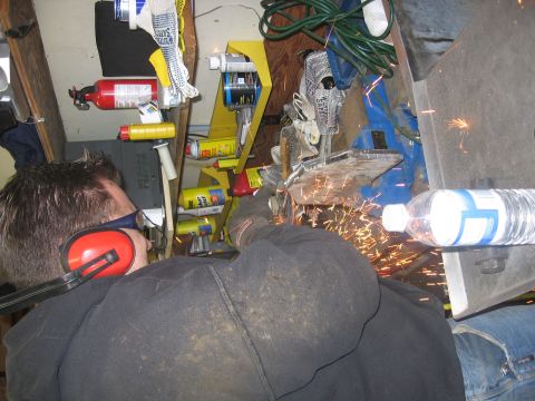 1989 Ford Bronco - A person is using an angle grinder, creating a shower of sparks, in a cluttered workshop environment.