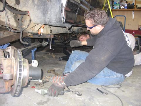 1989 Ford Bronco - Mechanics are working on the suspension and frame of a vehicle in a garage setting.