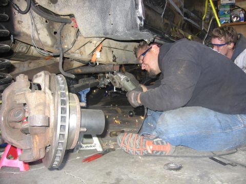 1989 Ford Bronco - Mechanics are working on the undercarriage of a vehicle, with one person using an angle grinder and sparks flying.