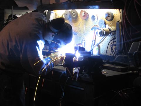 1989 Ford Bronco - Workshop scene with a person welding metal. Craftsman tools are organized on a pegboard in the background.