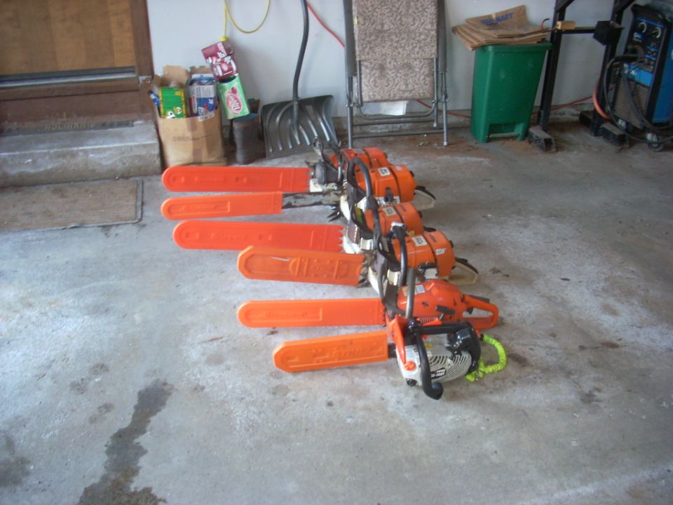 Several orange chainsaws lined up on a concrete floor