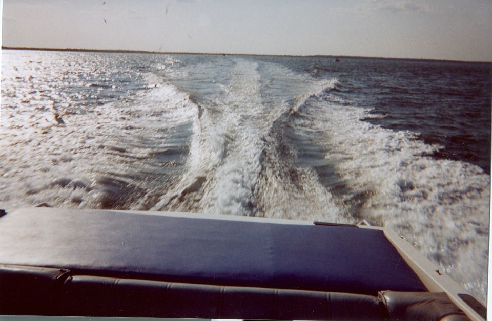 Boat wake trailing across open water seen from the stern with a vinyl cushion in view