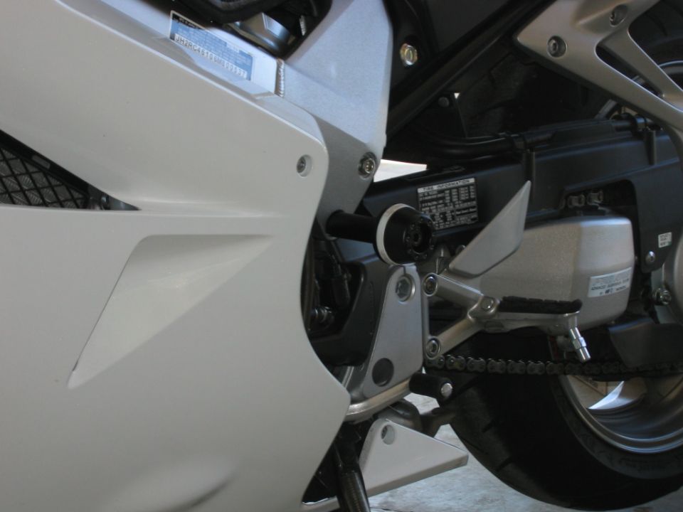 Motorcycle frame slider install, showing chain, footpeg, and frame decal
