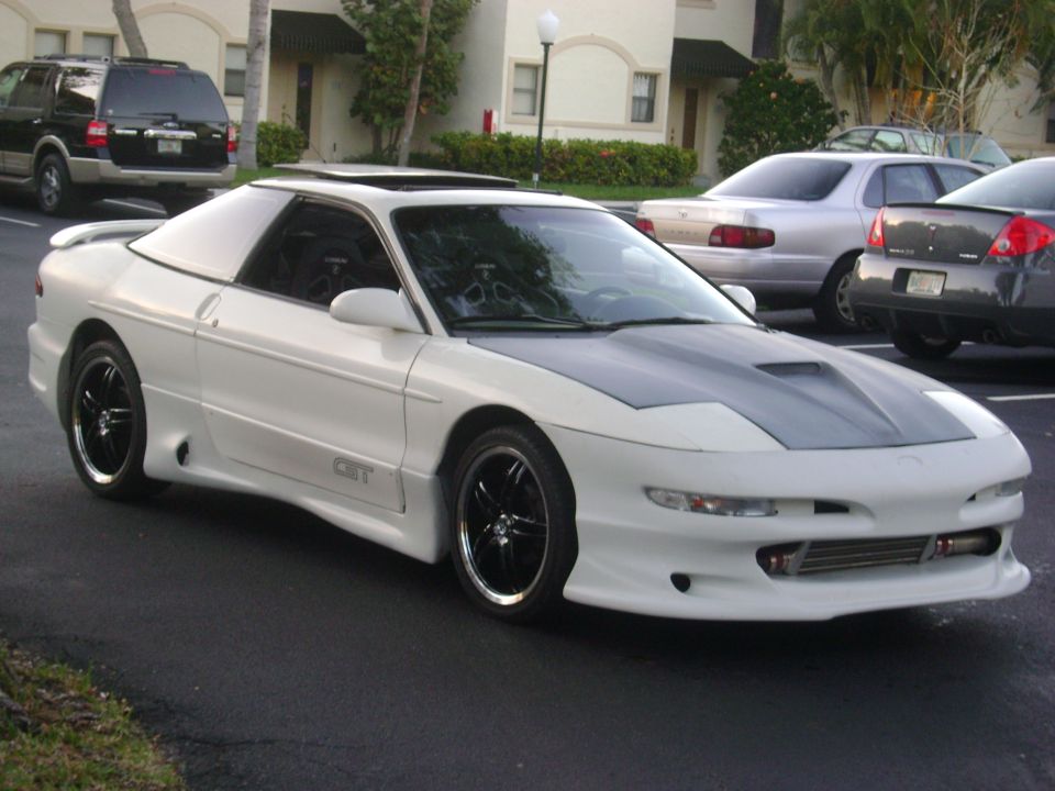 White 1994 Ford Probe with a grey aftermarket hood and custom side skirts, parked in a lot with other cars