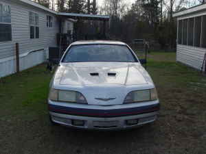 2004 Ford F-150 - A silver car with distinctive hood scoops is parked in a yard, with a Supermotors watermark visible.