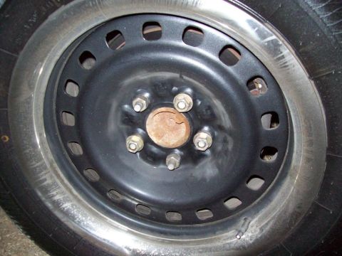2000 Mercury Grand Marquis - A close-up view of a black steel wheel, showing the lug nuts and a rusty center cap.