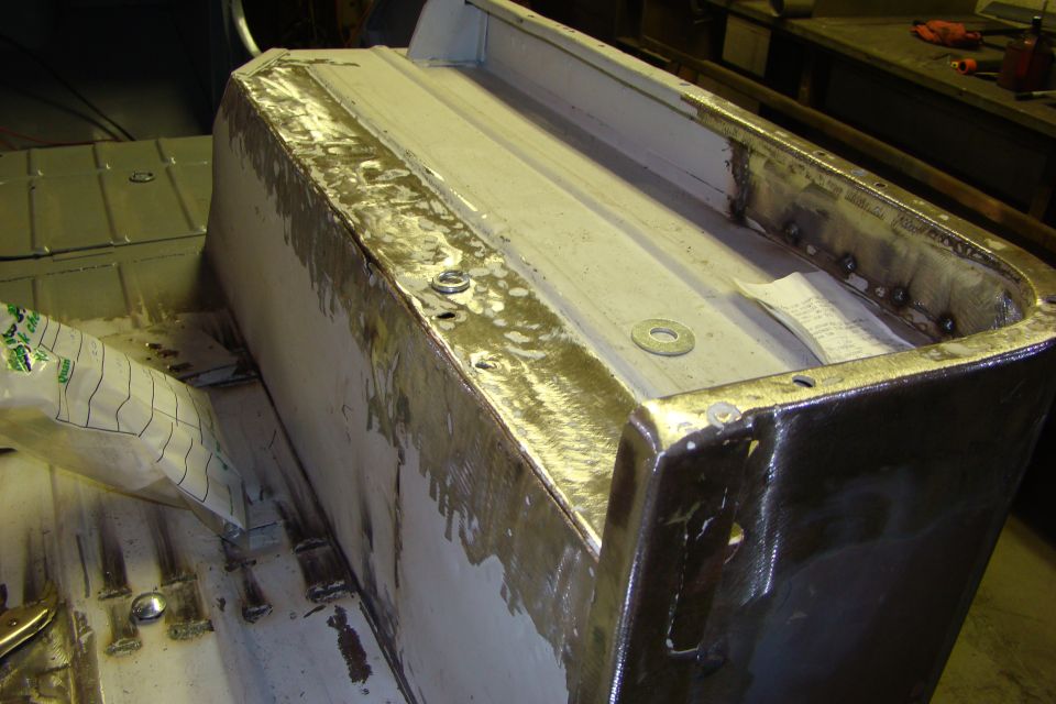 Close-up of a metal body panel with visible welds and some paper tucked inside
