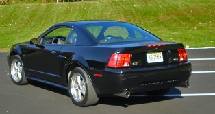 2002 Ford Mustang - Rear 3/4 view of a black 2002 Ford Mustang GT parked on asphalt with a grassy hill in the background.