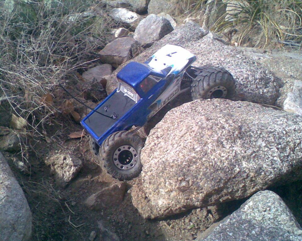 Blue RC crawler truck with large tires navigating a rocky terrain