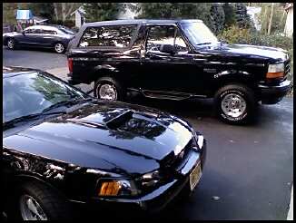 1996 Ford Bronco - A black Ford Bronco is parked next to a black car on a driveway.