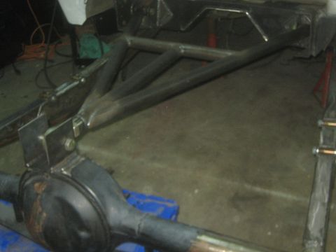 1990 Ford Bronco - fabricated tubular suspension A-arm and rear axle assembly sit on the floor of a workshop under construction.