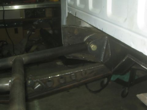 1990 Ford Bronco - Tubular suspension link arms and welded mounting brackets sit in front of a white vehicle body panel in a garage.