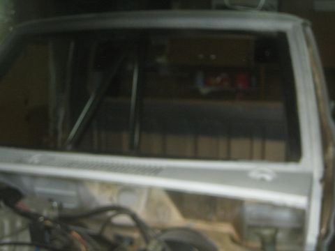 1990 Ford Bronco - rear window opening of a stripped, primer-coated vehicle body shows the bare interior during a build.