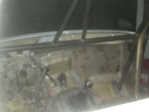 1990 Ford Bronco - stripped interior of a vehicle shows a roll bar, bare floor, shifter and exposed wiring during fabrication.