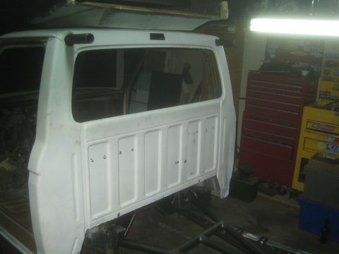 1990 Ford Bronco - white painted truck cab rear panel stands propped in a garage workshop alongside red tool chests.