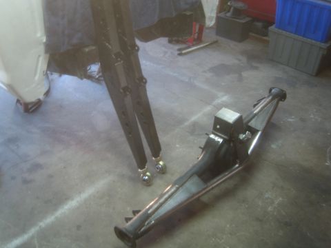 1990 Ford Bronco - fabricated tubular control arm with a bracket rests on the garage floor beside ladder-bar suspension links.