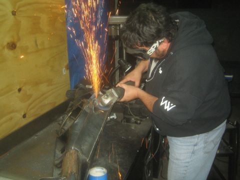 1990 Ford Bronco - Photograph of a fabricator grinding a fabricated steel part with sparks flying in a shop.