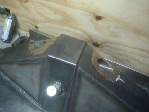 1990 Ford Bronco - Photograph of a fabricated steel suspension bracket with weld beads and mounting holes on a workbench.