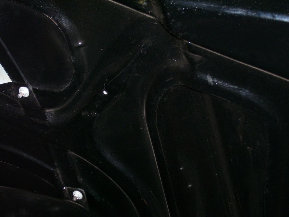 Close-up of the underside of a black car hood, showing structural details and mounting hardware.