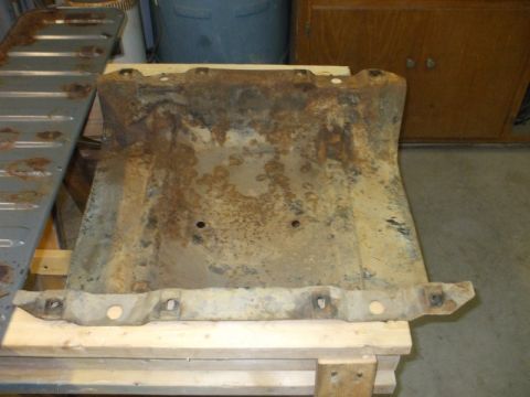 1995 Ford Bronco - A rusty stamped-steel floor pan section removed from a vehicle and laid across wood blocks on a shop floor, showing heavy surface corrosion…