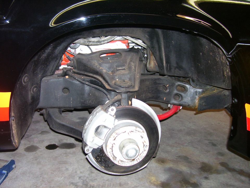 Close-up of black car's front suspension, brake caliper, rotor, and red sway bar.