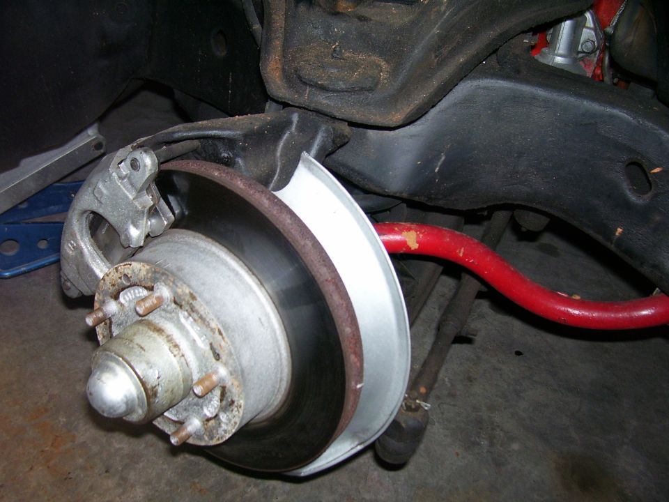 Vehicle front brake assembly with rotor, caliper, hub, and red sway bar.
