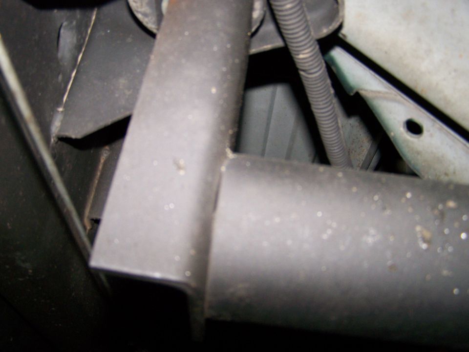 Undercarriage view of vehicle framing and a pipe, with a black ribbed conduit.