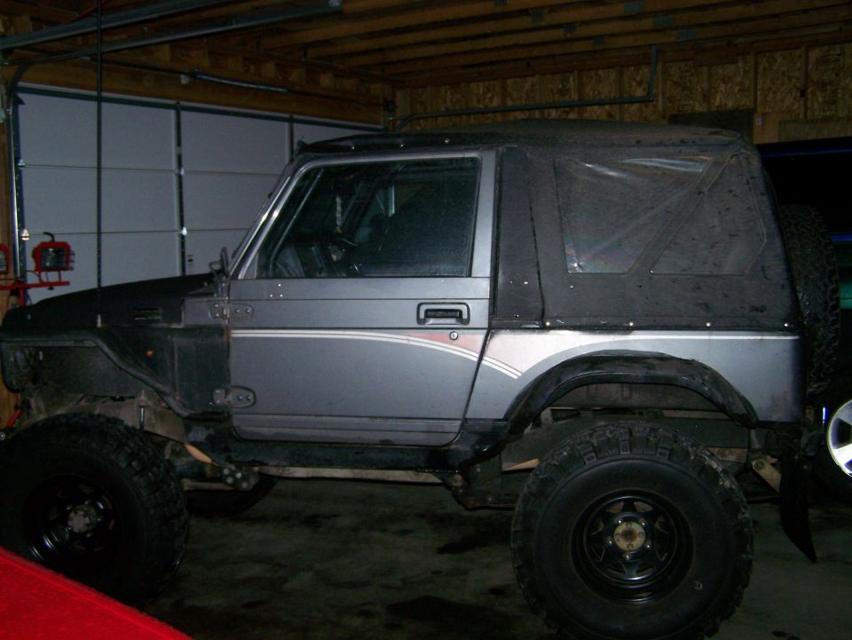 Modified gray Suzuki Samurai with soft top and large tires in a garage.