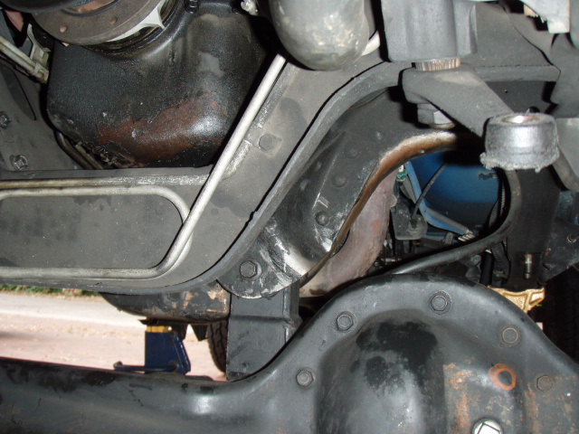 Underside of a vehicle showing differential, oil pan, exhaust, and a blue jack.