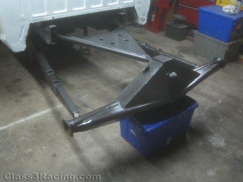 1990 Ford Bronco - Photograph of a black-painted tubular off-road suspension assembly mounted under a vehicle body in a shop.