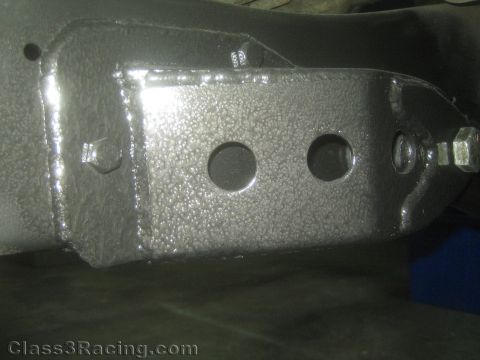 1990 Ford Bronco - Photograph of a wrinkle-coated fabricated steel suspension bracket with drilled holes and a bolt.