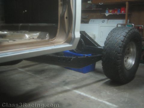 1990 Ford Bronco - Photograph of the rocker area and a fabricated black suspension link beneath a project truck in a garage.