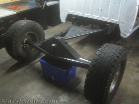 1990 Ford Bronco - Photo of a stripped truck frame and rear axle assembly on a shop floor, not a technical document.