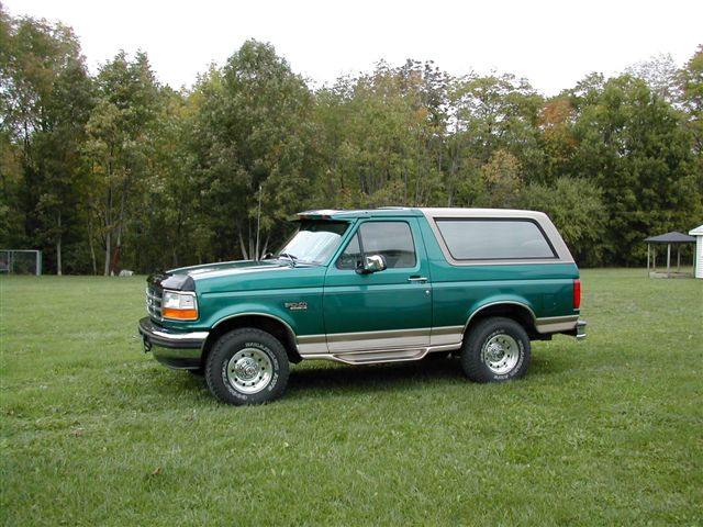 Green and tan stock Ford Bronco parked on a lawn, driver's side view
