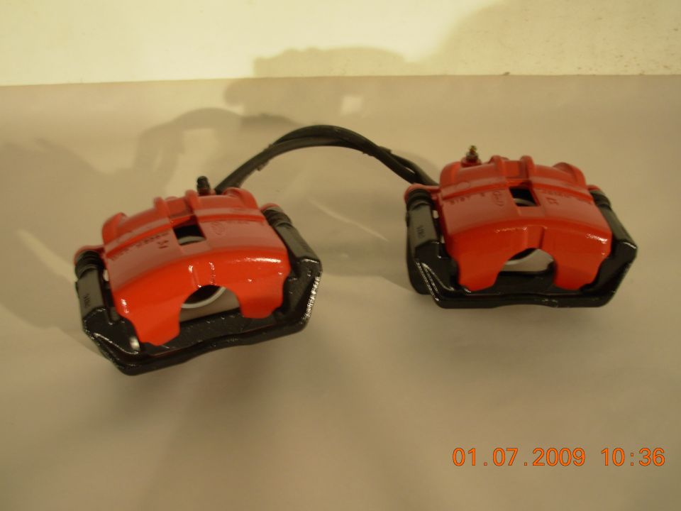Two red brake calipers with black hardware connected by a hose.